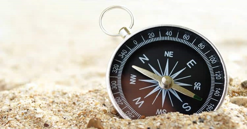 Fekete iránytű a homokba félig beágyazódva.