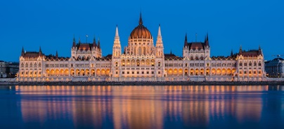 A budapesti Parlament épülete kivilágítva, a Duna vizének tükröződésével.