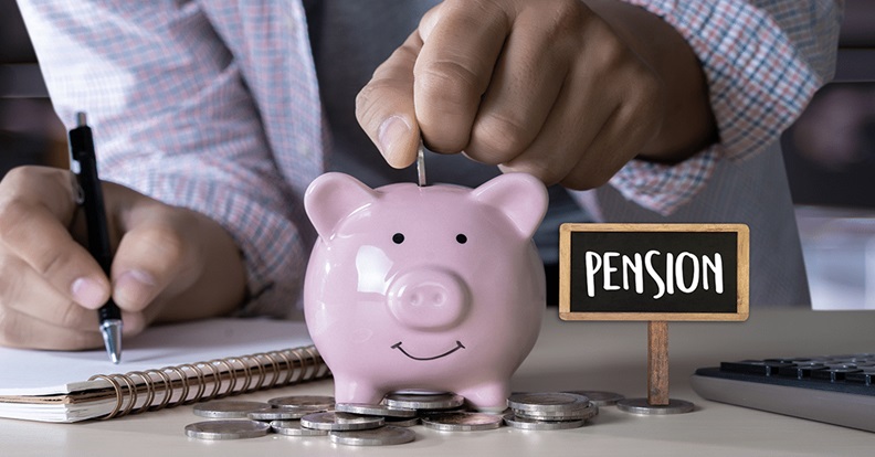 Rózsaszín malacperselybe érmét dobó kéz az asztalon szétszórt pénzérmékkel, mellette ‘Pension’ feliratú tábla, a nyugdíjcélú megtakarítást szimbolizálva.