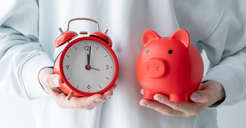 Két kéz egy piros ébresztőórát és egy piros malacperselyt tart.