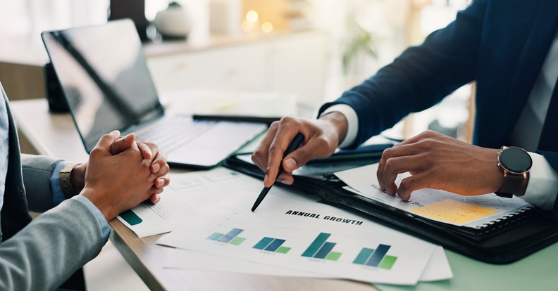 Pénzügyi elemzést végző szakemberek grafikonokat mutatnak és adatokat egyeztetnek egy üzleti megbeszélésen.