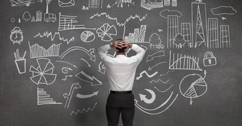 Egy üzleti öltözékű ember egy teli rajzolt fal előtt áll, amelyen grafikonok, diagramok és döntési folyamatokat jelképező nyilak láthatók, szemléltetve a befektetési döntések összetettségét és az információk túlterheltségét.